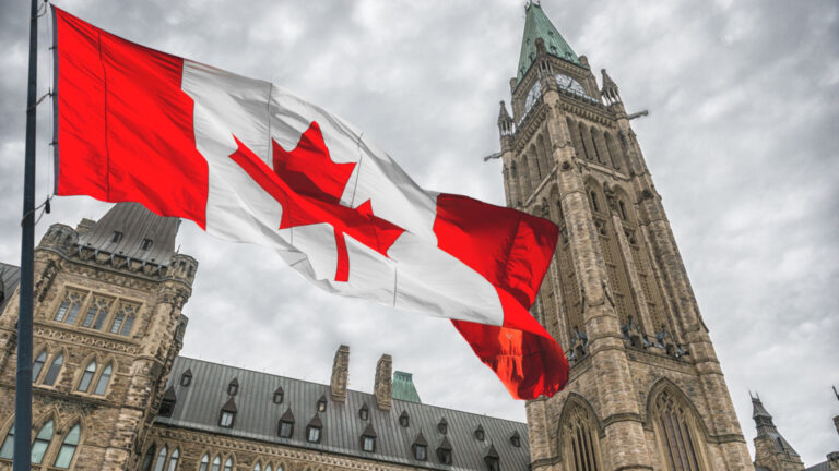 Un drapeau du Canada flotte au-dessus du Parlement. Des nuages gris assombrissent le ciel.