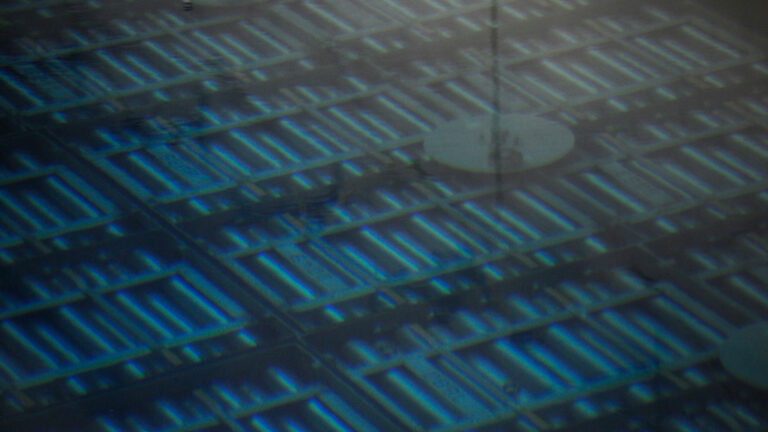 Rows of fuel bundles sit stacked under water. They are small metal cylinders. The water gives them a turquoise hue.