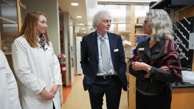 Three scientists, one in a white lab coat, chatting.