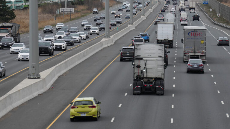 Eight lanes of traffic are shown. Most lanes are bumper to bumper. The green-and-white commuter train passes on tracks running parallel to the highway.