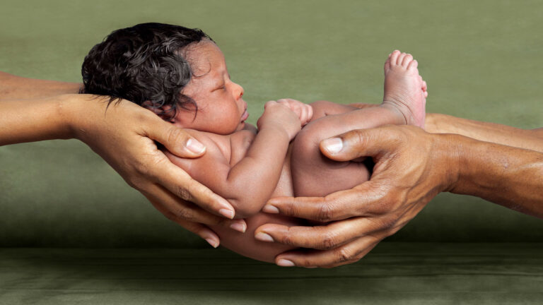 Four adult hands holding an adorable baby.