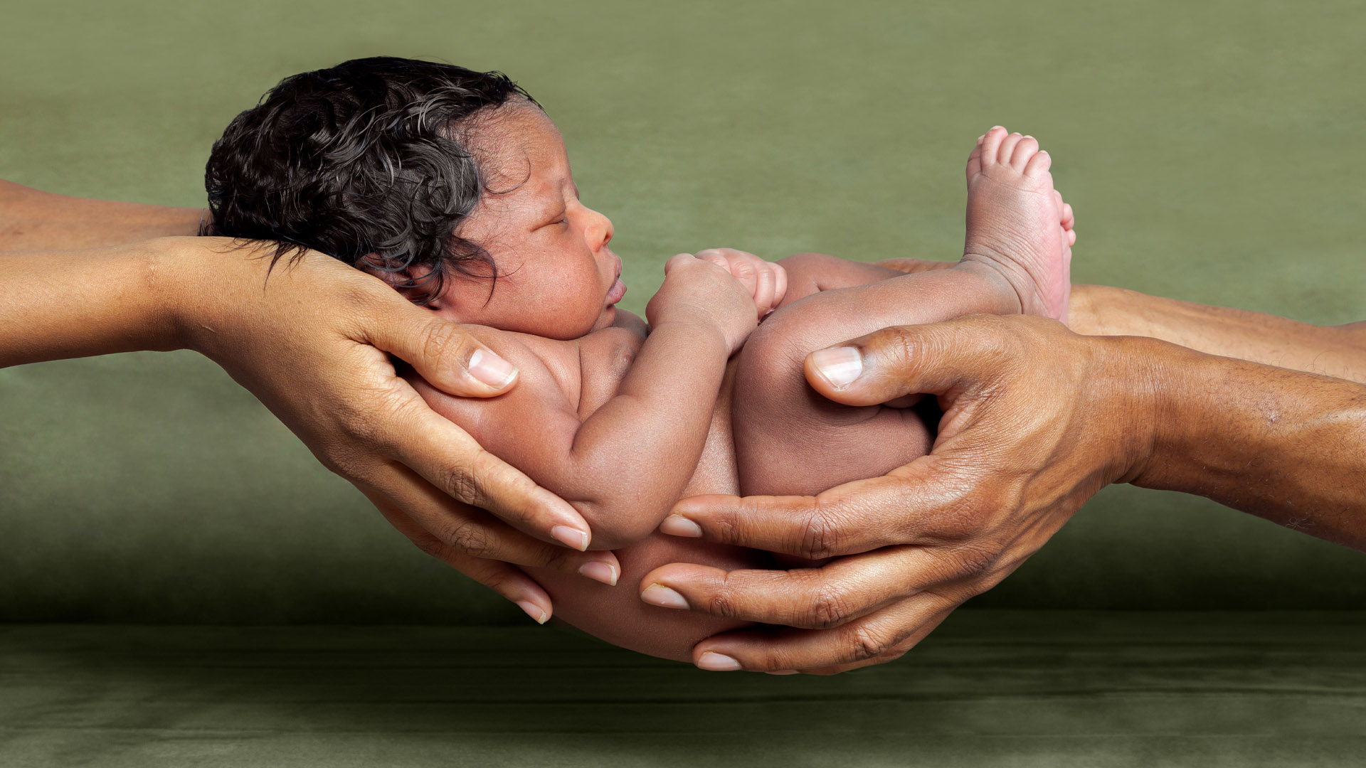 Four adult hands holding an adorable baby.