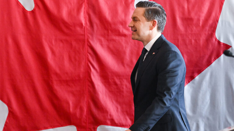 Pierre Poilievre traverse une scène avec un drapeau canadien en arrière-plan.