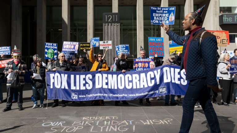 Des manifestants debout devant les bureaux de Fox News tiennent une banderole bleue sur laquelle est écrit en blanc «Fox Lies, Democracy Dies».
