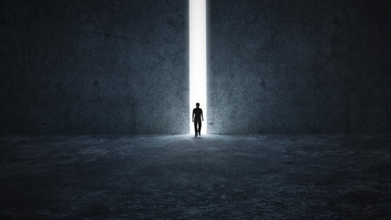 Une personne seule marche dans le noir vers une mince ouverture d’où jaillit une forte lumière blanche.