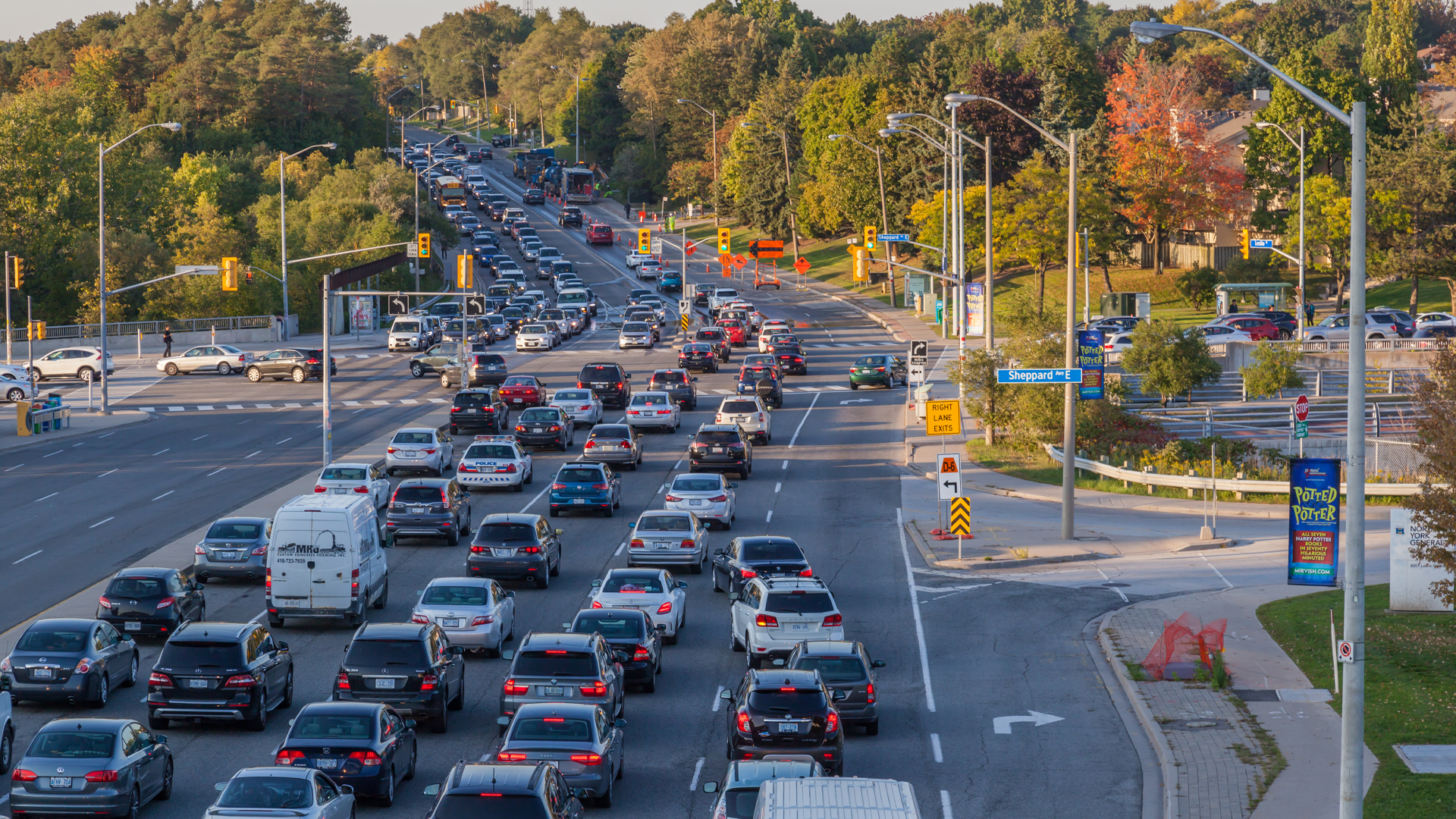 Five lanes of traffic on a road with dense stands of trees on both sides.