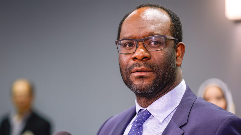 A close-up photo of Kaycee Madu at a microphone.
