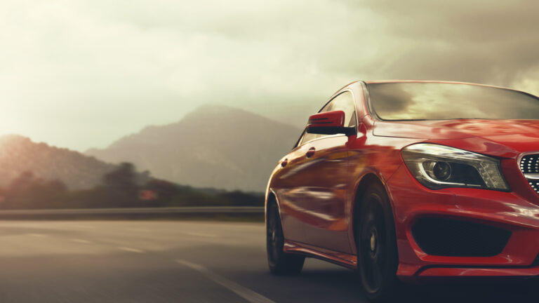 A red car drives on a winding road through a mountains.