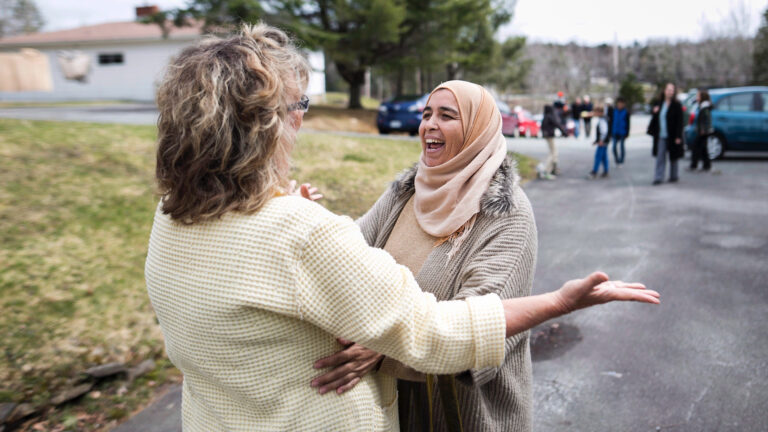 Two women are pictured on a street with their arms open moments before they embrace.