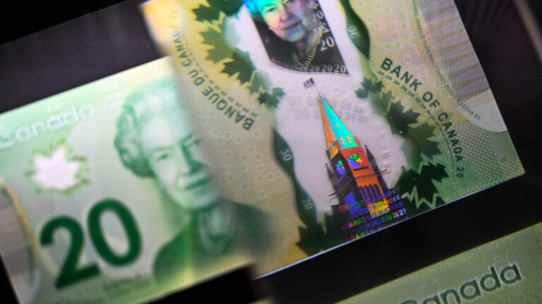 A magnifying glass enlarges the holographic image of Parliament Hill's Peace Tower on a $20 bill.