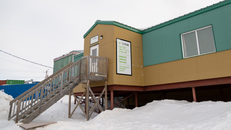 The centre is a long, one-storey building in shades of green and brown, with a wood set of stairs. It’s surrounded by snow.