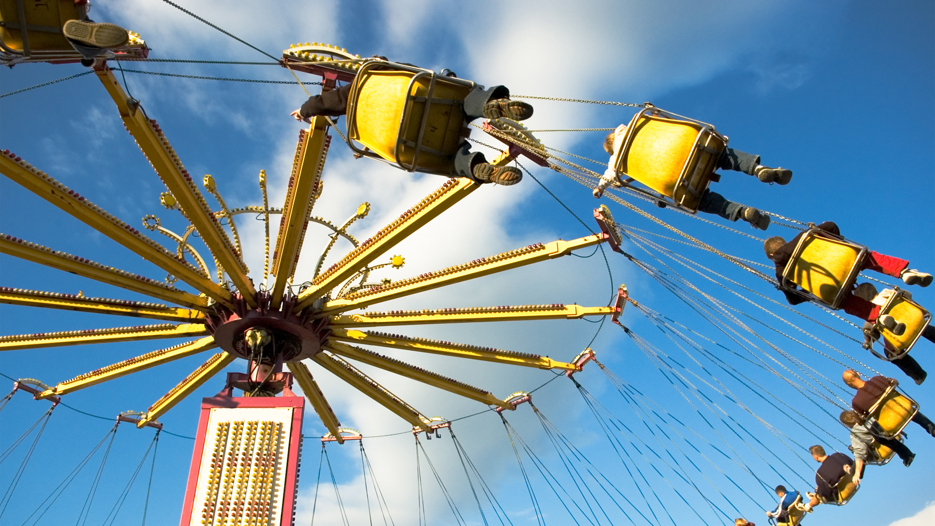 People ride a swinging carrousel carnival ride against a blue summer sky.