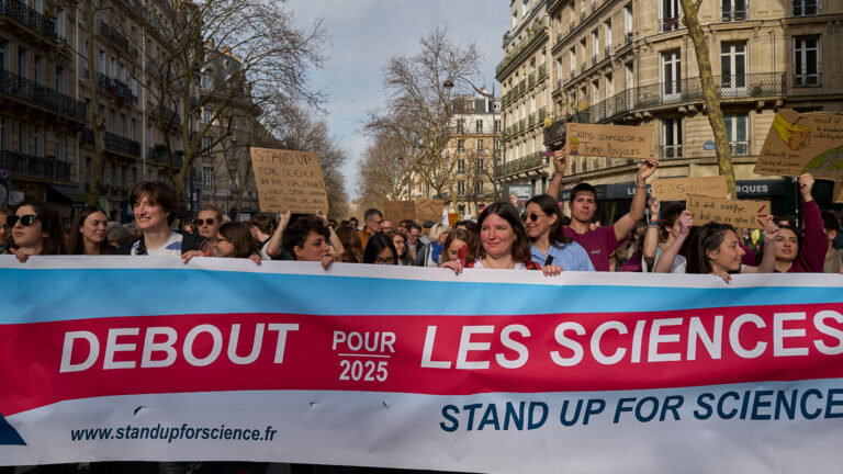 Des manifestants avancent dans la rue en tenant une banderole sur laquell est écrit : Debout pour la science.