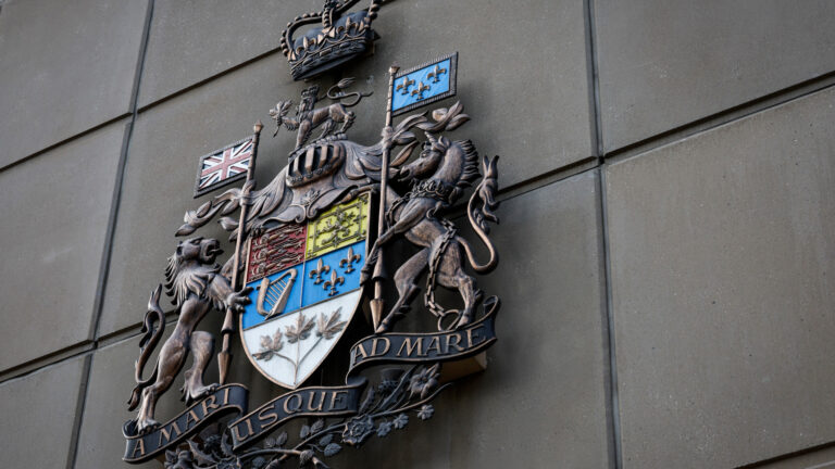 The metal crest is ornate with elements that include depictions of the fleur-de-lys, a harp, maple leaves, the Union Jack flag and a crown at the top.