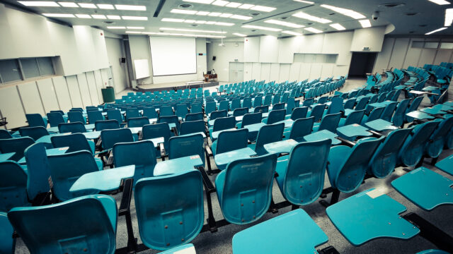 An auditorium with dozens of rows of turquoise desks side by side.