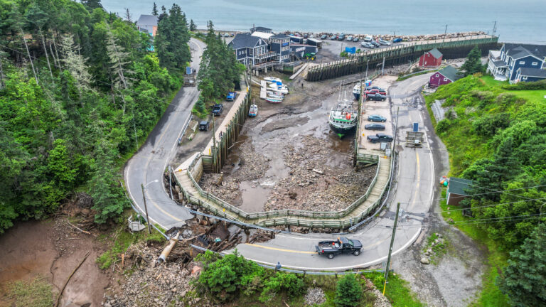 A broken winding highway with a small marina with a boat sitting on land inside one of the highway curves. The ocean is in the background.