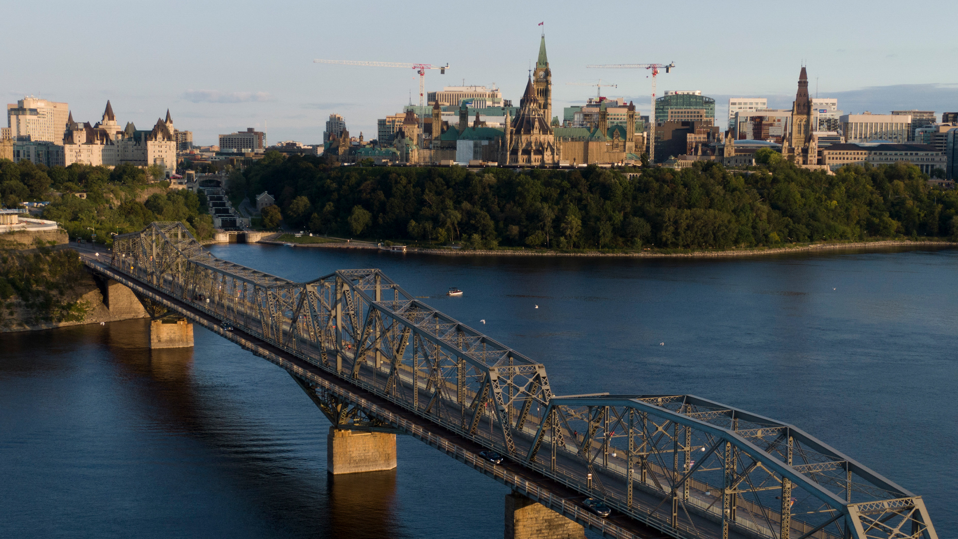 A view of Parliament Hill with two construction cranes with the Alexandria Bridge in the foreground taken from a drone above the Outaouais River.