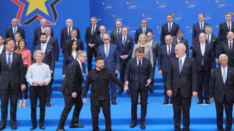 About 40 leaders standing in about four rows in front of a blue backdrop. Ukrainian President Vladimir Zelenskyy is in the foreground directing traffic.