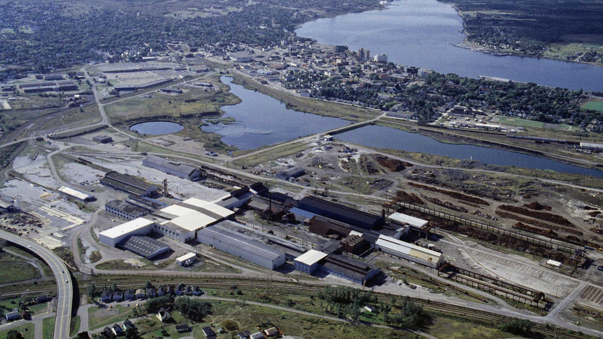 Vue aérienne de l'usine, avec son groupe de bâtiments longs et bas et les bassins de goudron situés à proximité des quartiers résidentiels de Sydney.