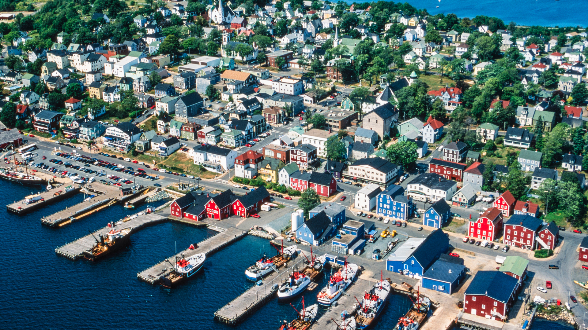 An aerial photo of the town shows the street grid of the commercial and residential areas bordered by an inland waterway on one side and the harbor on the other, with eight jetties dotted with ships and sailing vessels. Some of the waterfront buildings are bright red or blue.