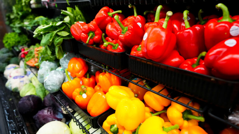 Red, orange and yellow peppers and other vegetables are shown in the grocery store produce aisle.