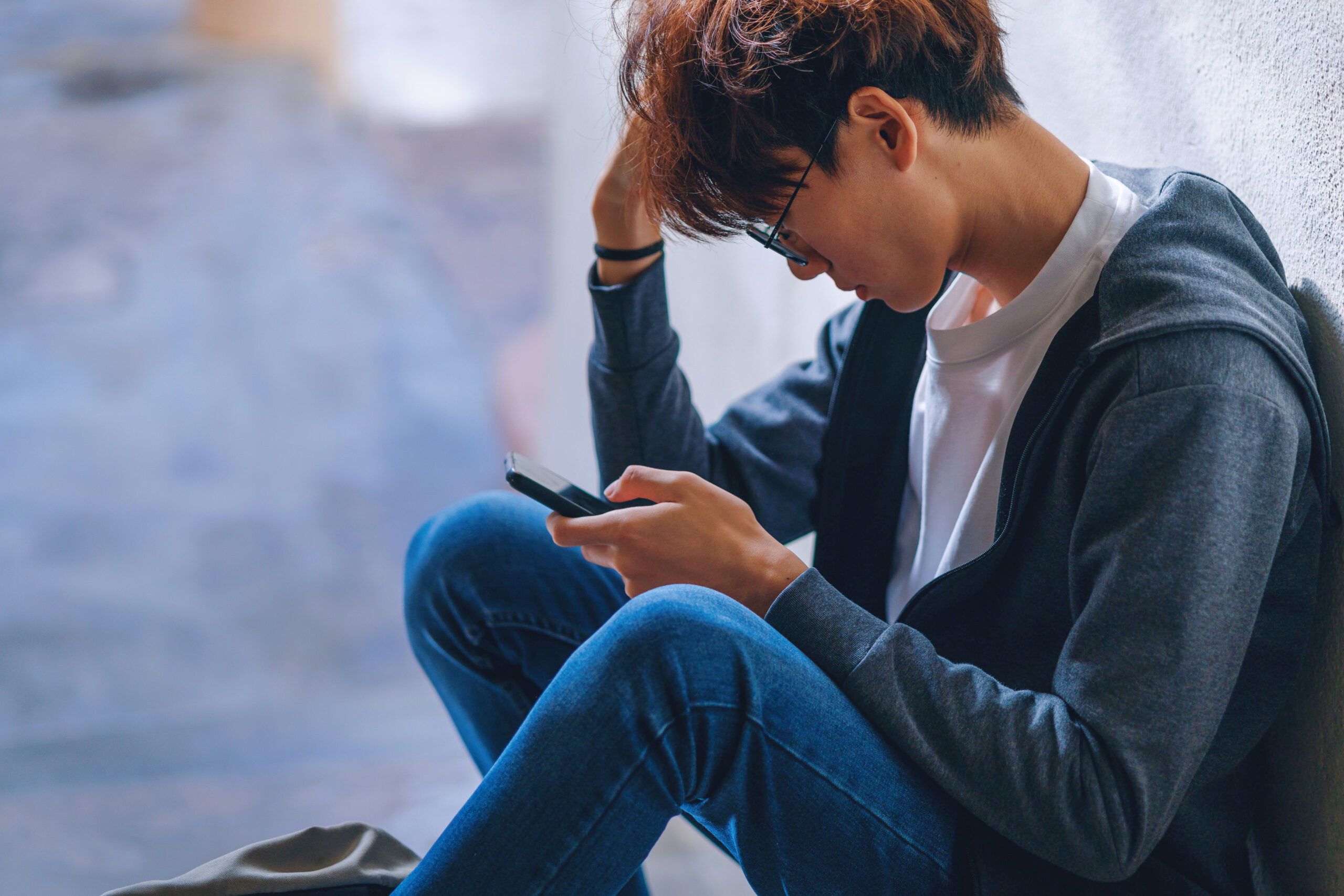 Un jeune homme est assis seul et a les yeux fixés sur son téléphone.