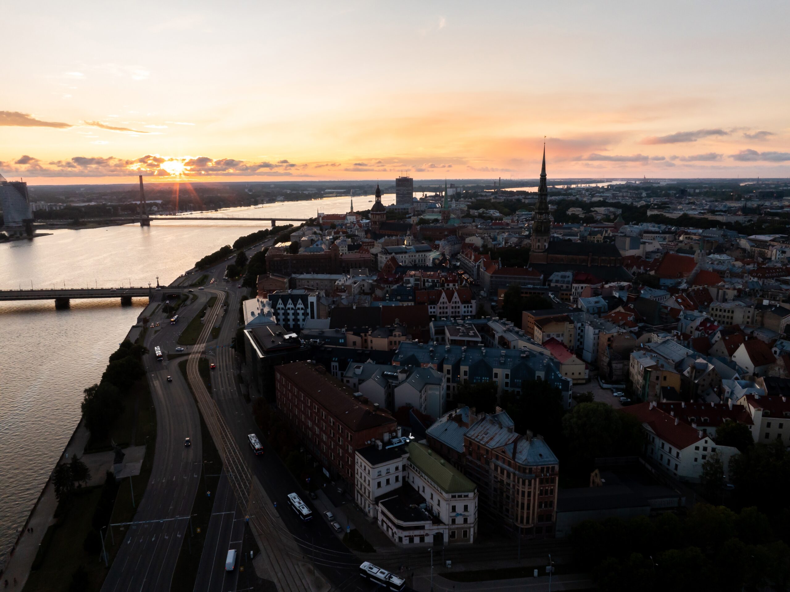 The river curves to the right and has two bridge crossings. The town is in shadow as the sun sets close to the horizon in the distance.