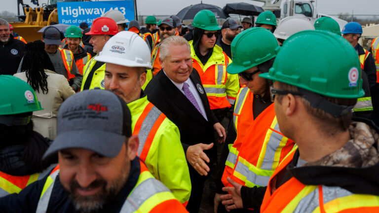 Doud Ford, wearing a dark suit, shakes hands with workers in hard hats and reflective vests.
