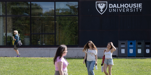 Four students are walking on the lawn in front of a black building with a “Dalhousie University” sign.