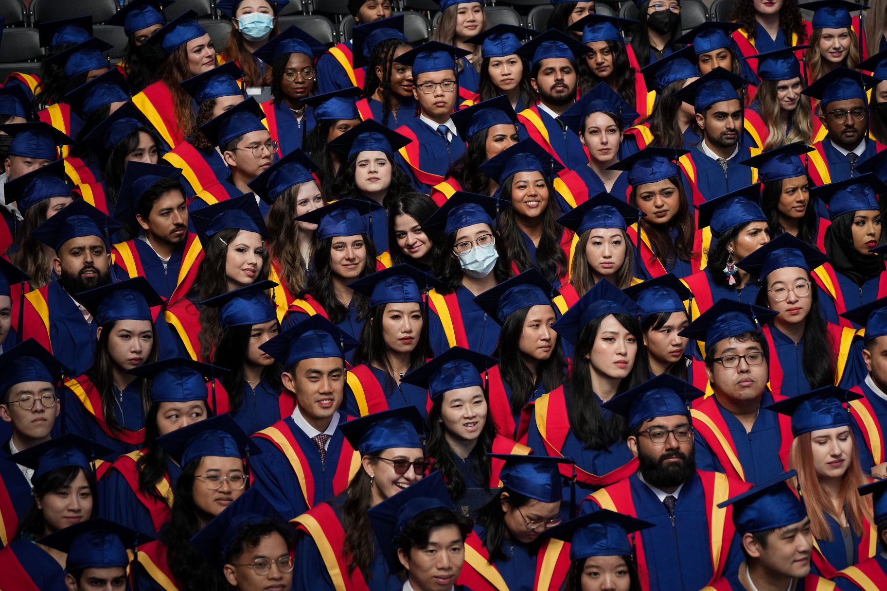 A diverse crowd of university students in blue cap and gown.