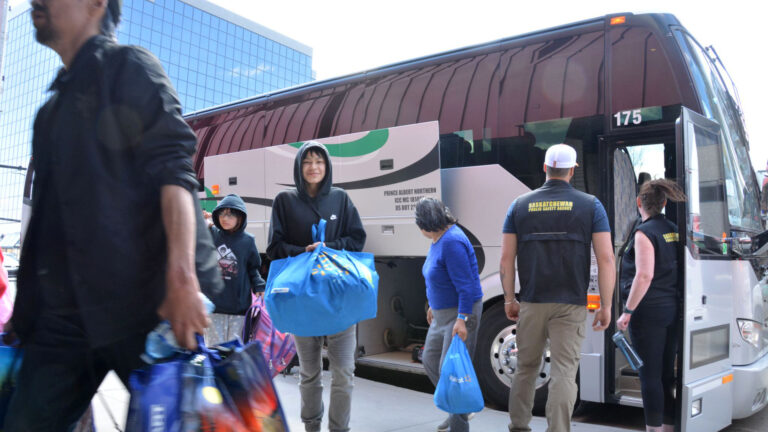 Four people carry stuffed bags from the bus after being evacuated after the wildfire in Saskatchewan