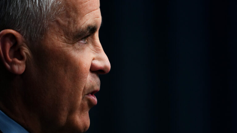 Closeup of Carney’s face in profile, set against a black background.