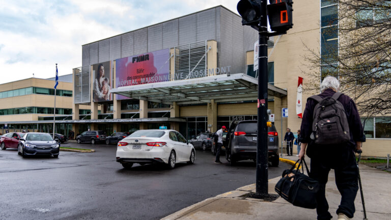 Main entrance of Maisonneuve-Rosemont Hospital in Montreal, with cars in front of the pavilion and a man walking with a cane and a travel bag, seen from behind.