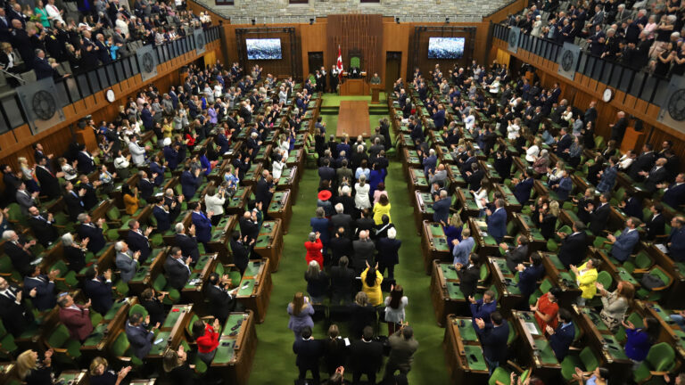 Wide view of Canada’s House of Commons filled with MPs standing and applauding during a parliamentary session in Ottawa.