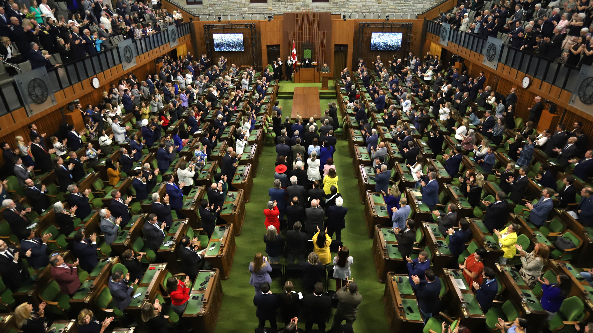 Vue d’ensemble de la Chambre des communes du Canada remplie de députés debout et applaudissant, lors d’une séance parlementaire à Ottawa.