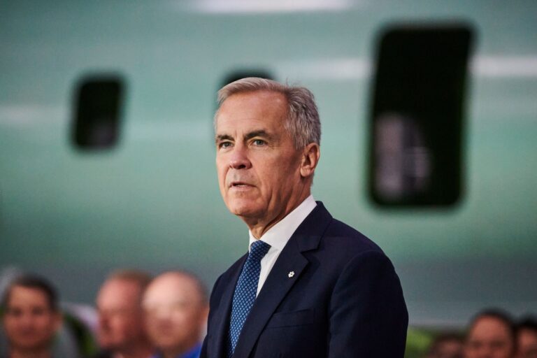 Carney is in front of the side of a passenger jet, with a few other people in the background.