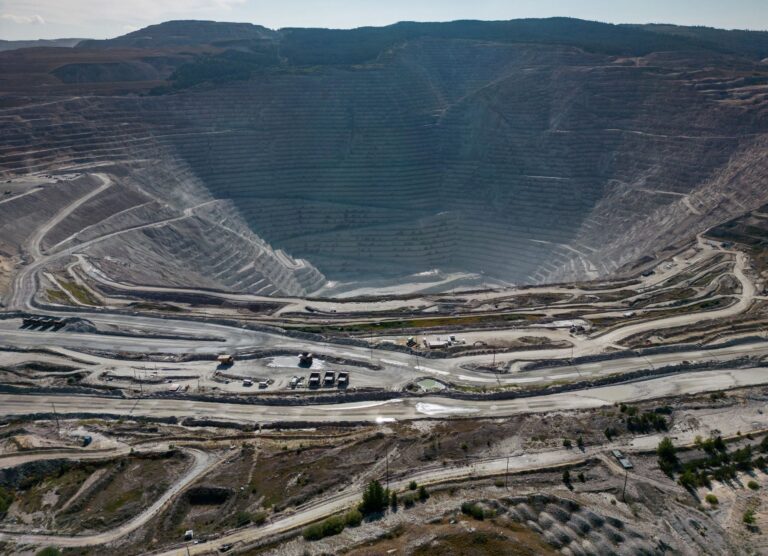 Dirt roads ribbon a brown landscape in the foreground with a large terraced open pit cut into the ground in the background.