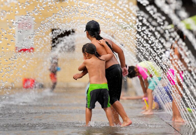 Two small children tussle under an arc of water.
