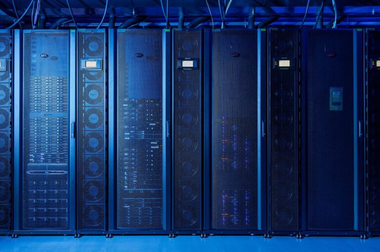 A blue light covers a bank of tall, narrow electronic computing boxes with wires coming out of the top.