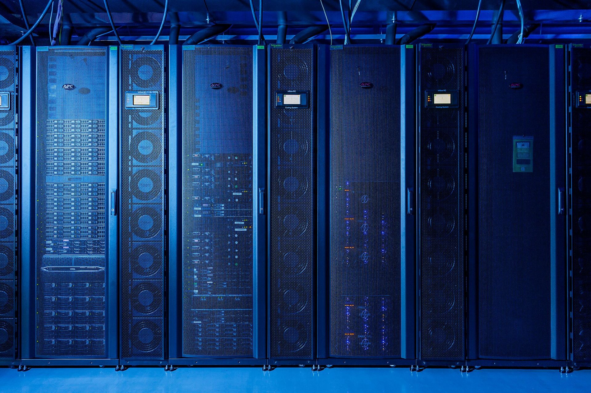A blue light covers a bank of tall, narrow electronic computing boxes with wires coming out of the top.