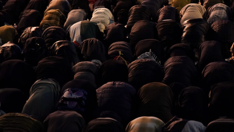 Lines of people bent over in prayer at night.