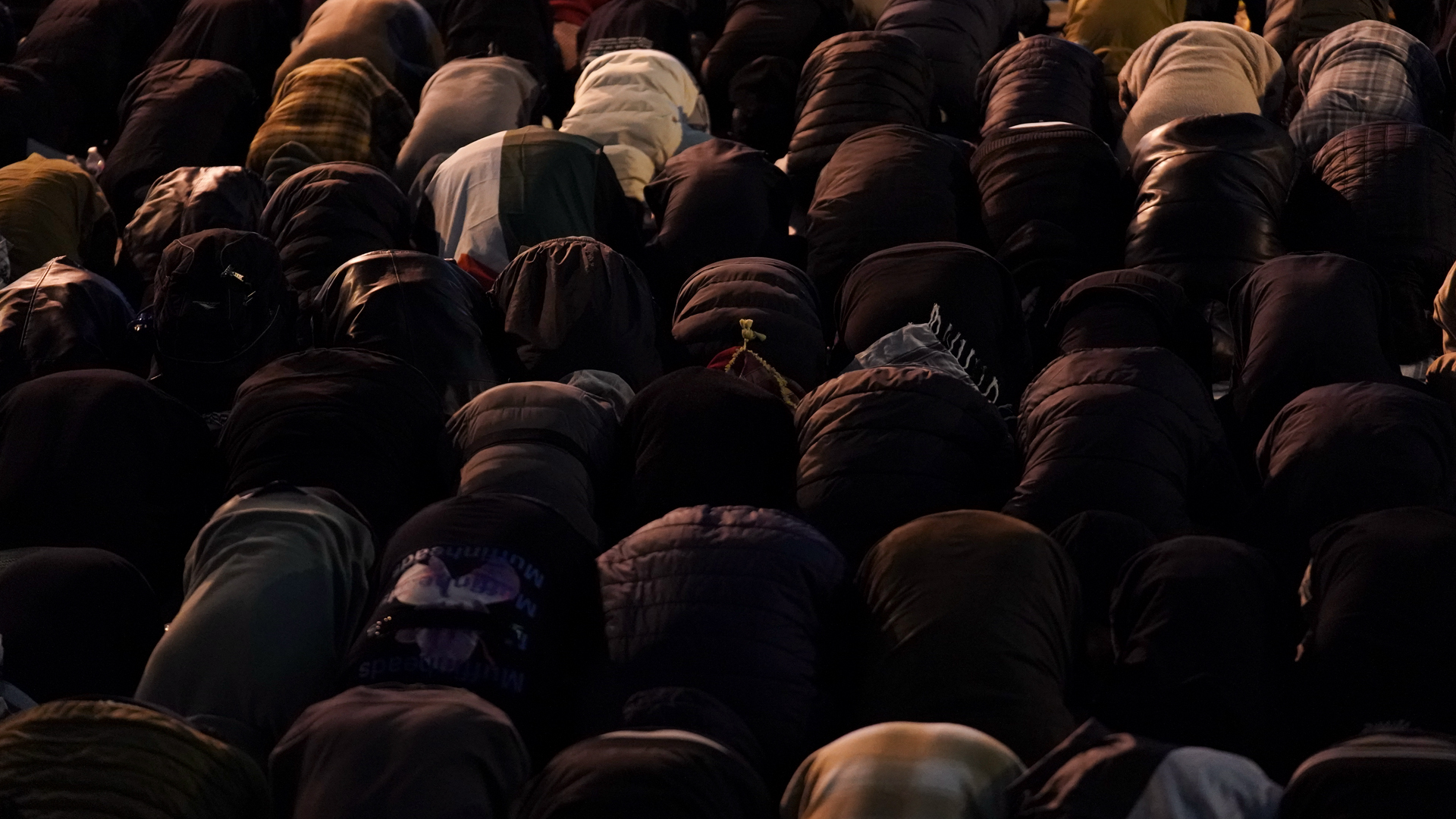 Lines of people bent over in prayer at night.