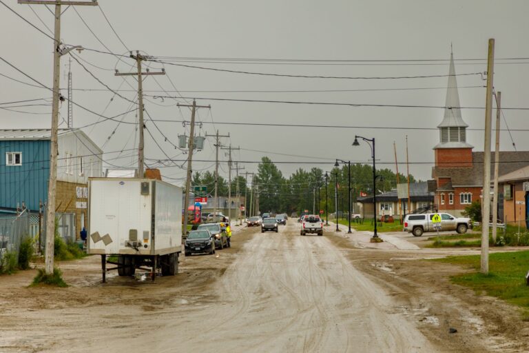 The street is unpaved and lined with low-rise brick buildings, a church and lots of electrical poles and overhead wires.
