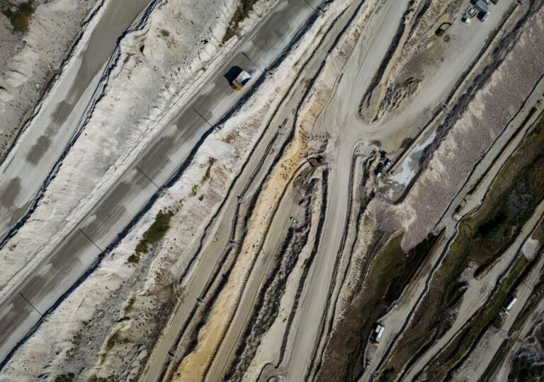 An overhead image of a mine with a dump truck navigating a ribbon of roads and ridges in various shades of beige and grey.