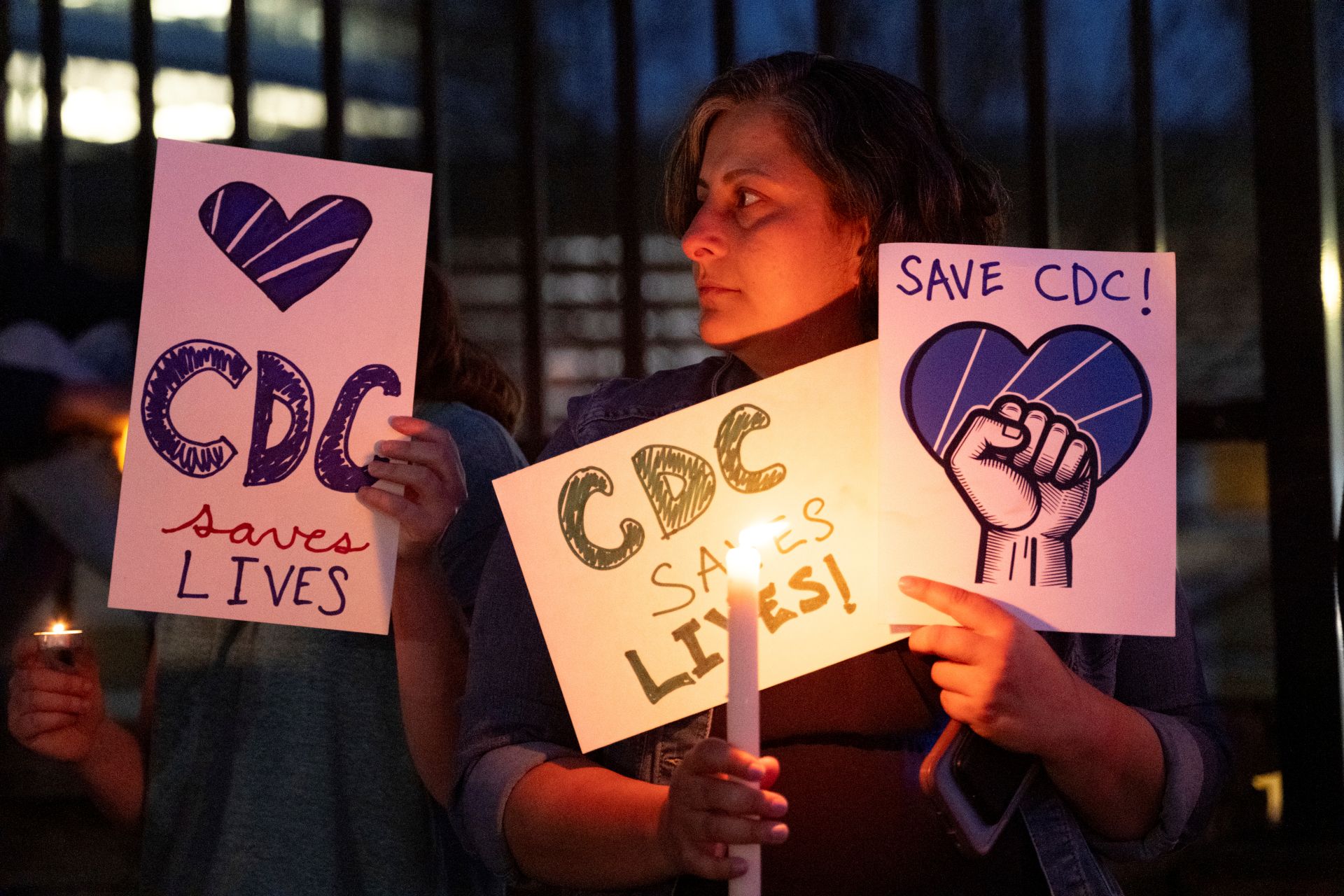 A woman holds a lit candle with signs that say “Save the CDC” and “CDC saves lives.”