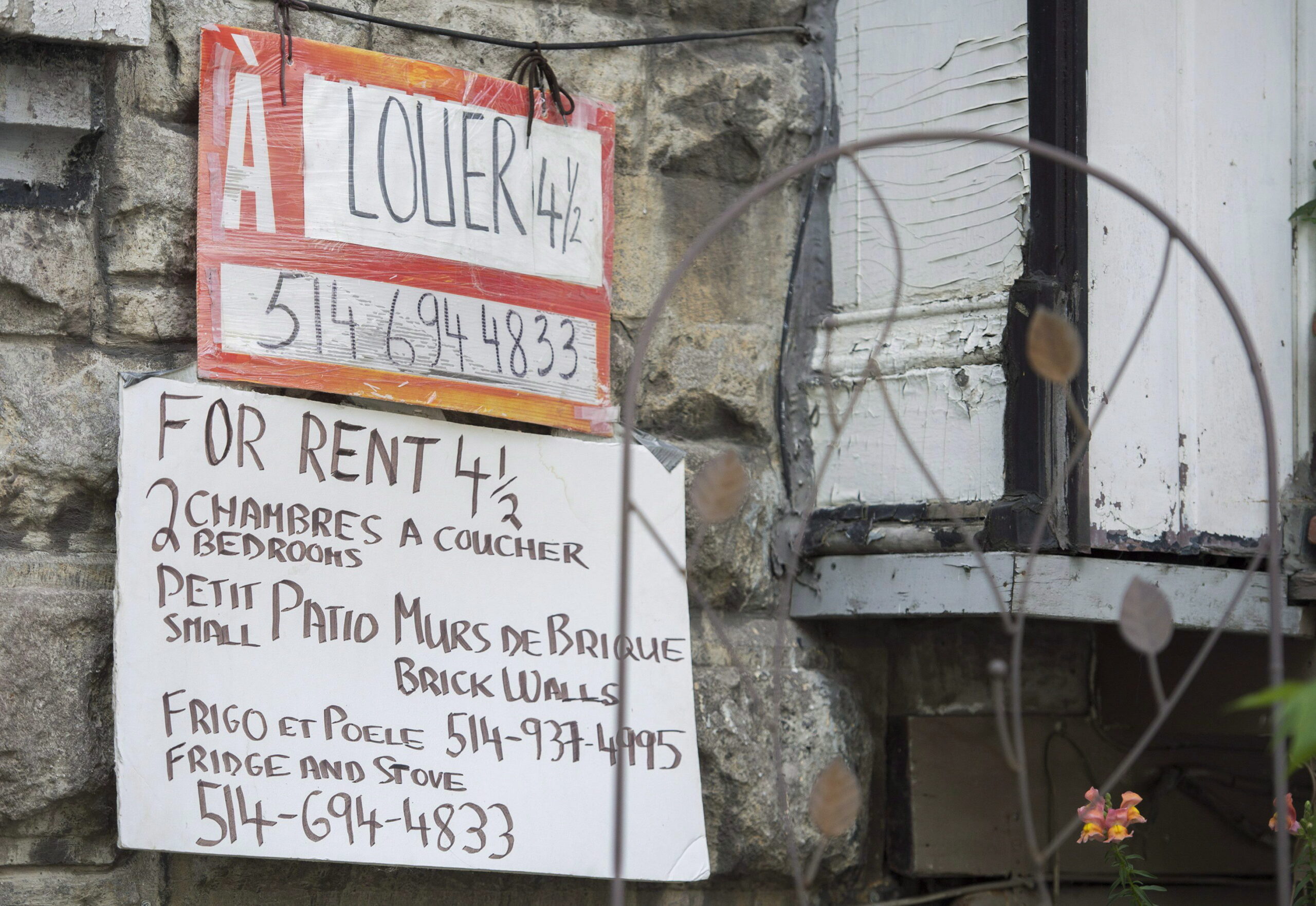 façade en pierre d’un immeuble avec deux affiches annonçant un logement 4 ½ à louer. L’une est une pancarte orange « À louer », l’autre une affiche manuscrite donnant des détails.