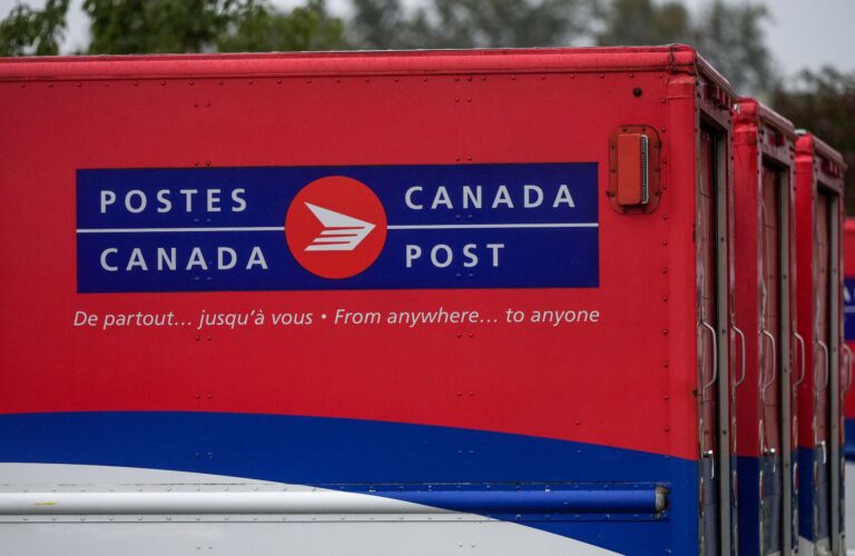 A line of Canada Post red, blue and white trucks with the slogan “de partout . . . jusqu’à vous” and “From anywhere . . . to anyone” written on the side.