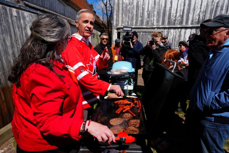 Mark Carney wearing a Team Canada sweater while working the BBQ with some supporters.