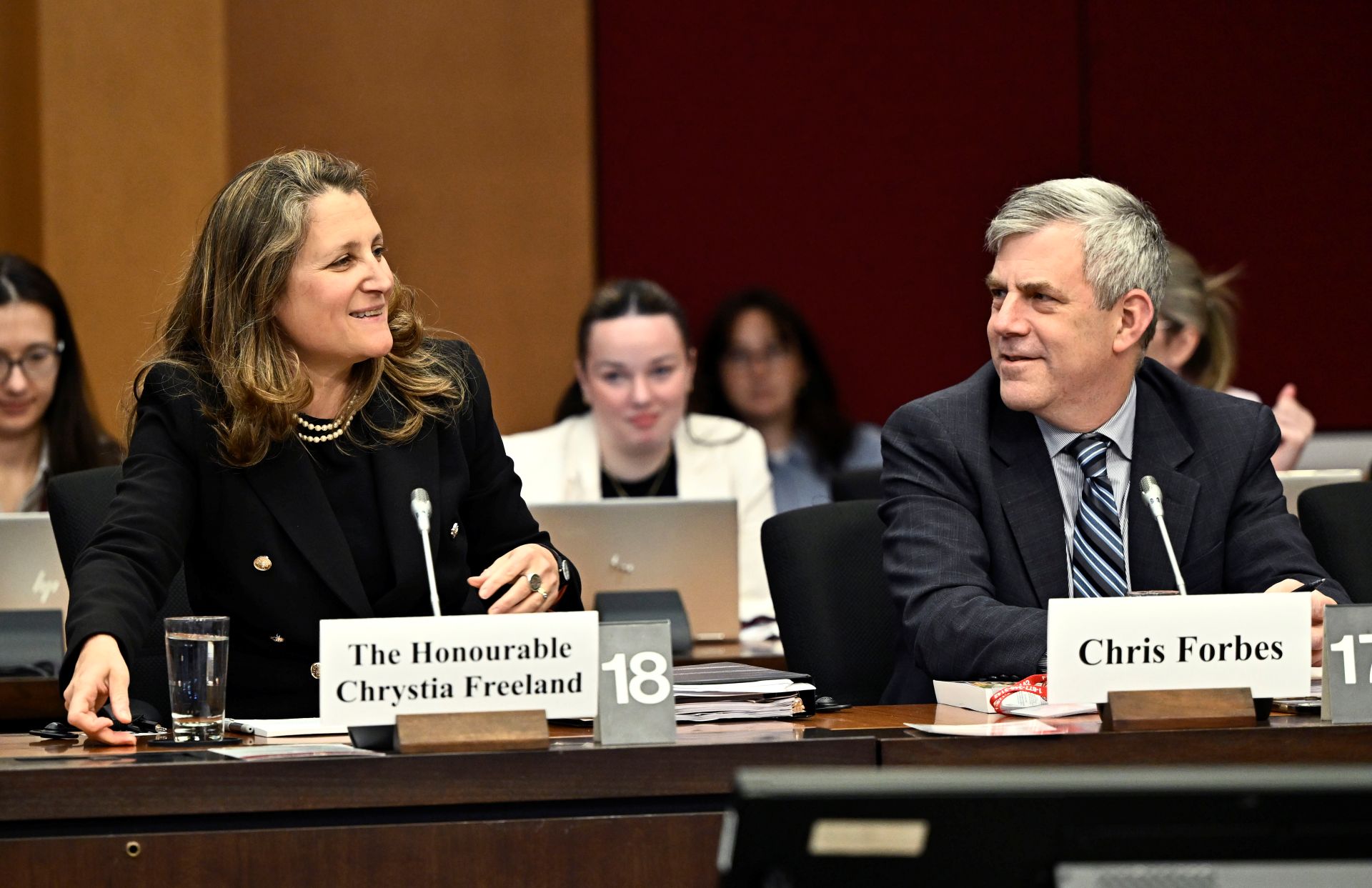 Forbes sitting next to Freeland at a committee table. 

