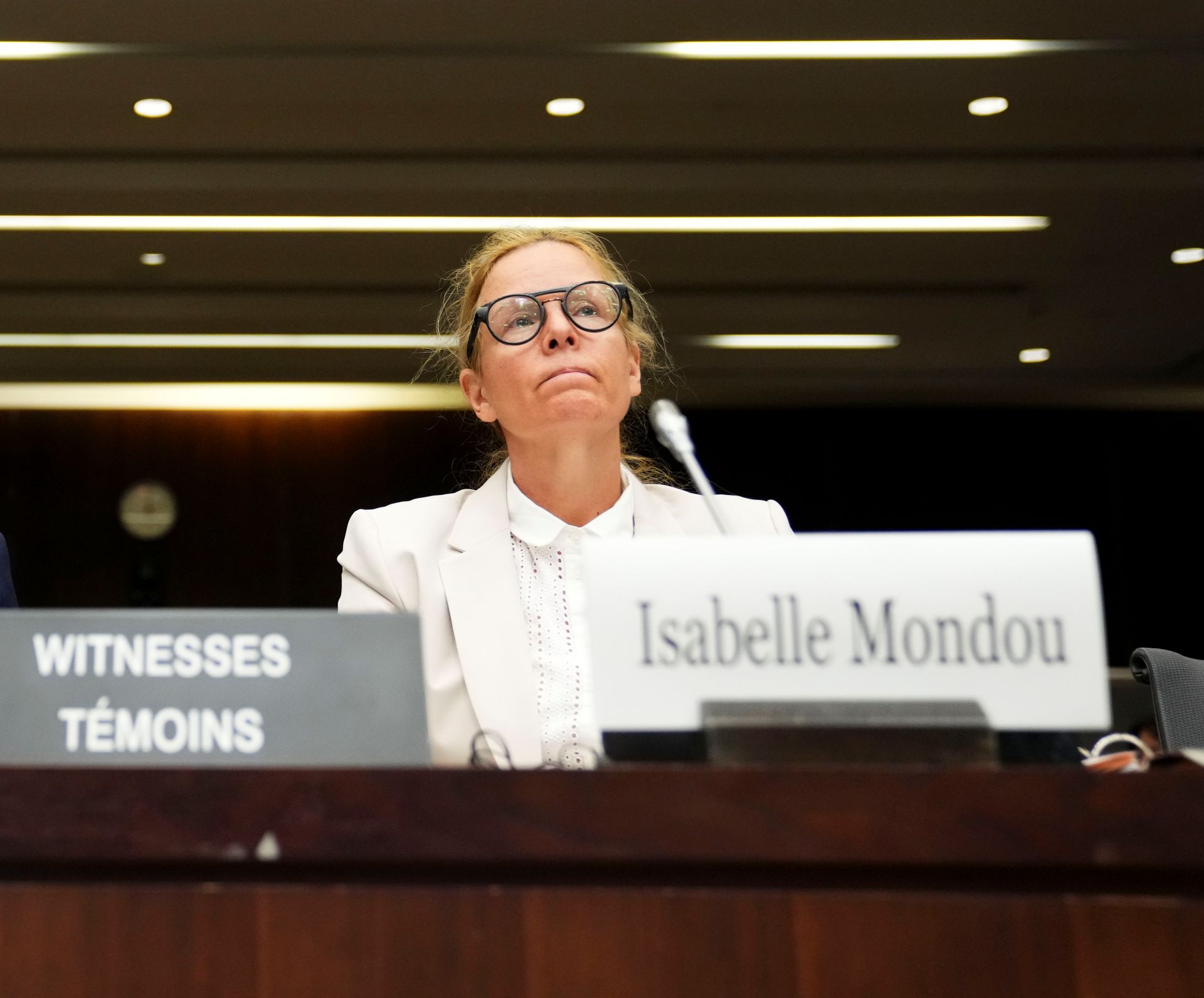 Mondou sitting at a hearing table with a microphone and her name plate in front of her. 